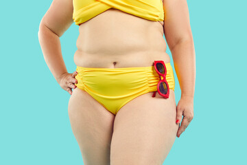 Crop shot of overweight, obese woman with fat belly wearing yellow bikini bottom and bra with red...
