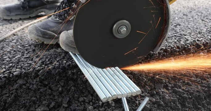 A metal worker cuts a threaded metal bars with an angle grinder.