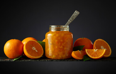 Orange jam in glass jar and fresh fruits on a black background.
