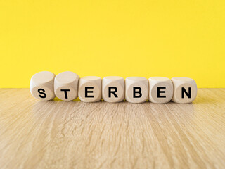 Wooden cubes with the German words 'Sterben' (die) and 'erben' (inherit). Beautiful wooden table,...