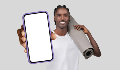 Black man standing while holding a yoga mat in one hand and a cell phone in the other. He appears...