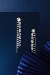Diamond earrings on a blue background. Beautiful and expensive jewelry. Top view.