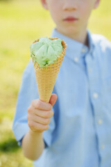 Unrecognizable child in shirt holds ice cream in waffle cone in his hands on sunny summer day....