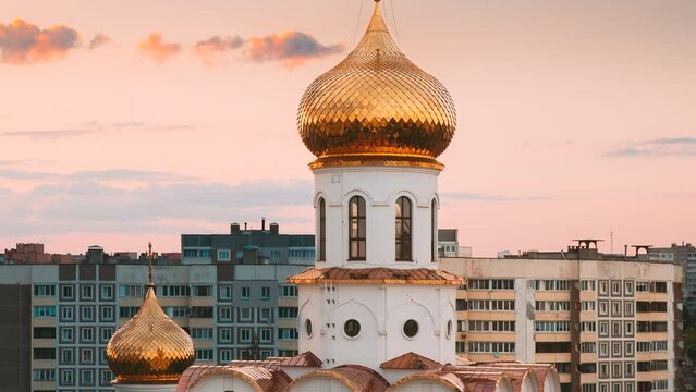Church In City At During Sunset Time. Gold Reflections At Domes. Summer Sunset Orange Cloudy Sky Background. Temple And Multi-storey Houses. Urban View. Bold Dramatic Sky Hyperlapse. Tranquility View.