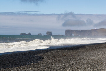 waves crashing at the black sand beach of Reynisfjara with an stunning mountain range in the...