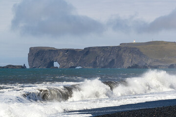 waves crashing at the black sand beach of Reynisfjara with an stunning mountain range in the distance, Iceland