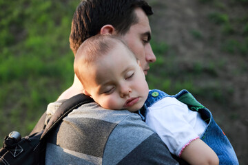 Portrait of little adorable sleeping girl and her father holding her in spring outdoors