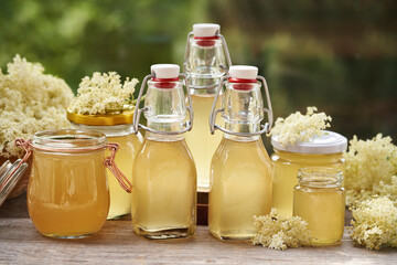 Several bottles and jars of homemade elderberry flower syrup outdoors in a garden