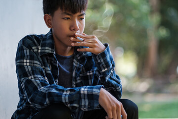 Teenagers underage smoking a cigarette causes bad habits causing addiction. Asian kid smoking behind the school toilet, an old dirty grungy place.