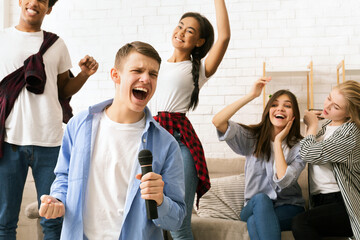 A diverse group of friends standing together on a stage, singing into a microphone, dressed in casual clothing and are passionately performing for an audience