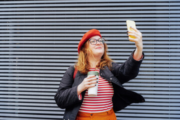 Smiling confident redhead plus size woman taking a selfie photo outdoors. Emotional hipster fashion...