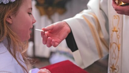Young Caucasian Catholic Girl in White Alb Festive Outfit Receiving First Holy Communion Sacrament From Catholic Priest