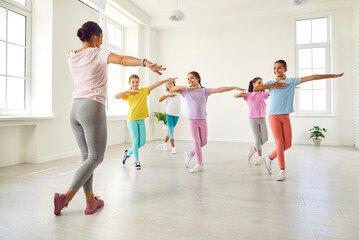 Happy children dancing. Group of little girls in sporty casual clothes are dancing in choreography class. Preteen girls rehearse dance moves with their female coach at children's dance studio.