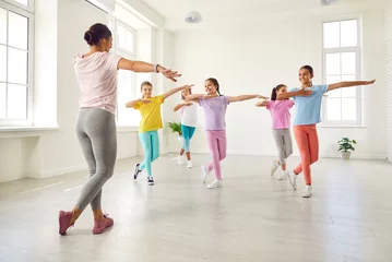 Fotobehang Happy children dancing. Group of little girls in sporty casual clothes are dancing in choreography class. Preteen girls rehearse dance moves with their female coach at children's dance studio. © Studio Romantic