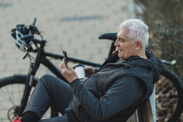 Man Sitting on Bench Next to Bike and Using Smartphone