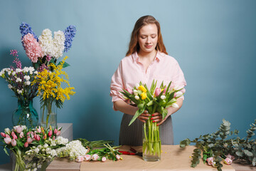 girl florist collects a bouquet of spring tulip flowers on a clean blue background