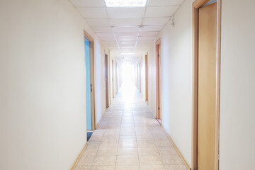 Empty corridor in a hospital with open doors to the rooms and a bright light at the end of the...