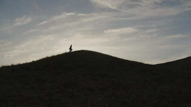 Silhouette of a man running towards the top of a hill against the sky. A man in a suit masters the top.