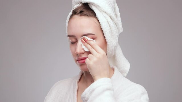 A young beautiful girl removes makeup with a cotton pad and micellar water from her face and eyes.