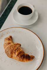 Cup of black coffee and a croissant on a table in a street cafe.