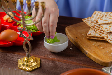 The hand of Jewish women dips maror into salt water at the Pesach Seder table