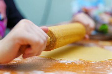 Hands rolling dough with a wooden rolling pin