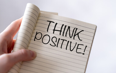 A hand holding an open notebook with the words Think Positive written on it. The image conveys...