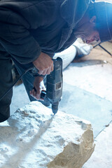 A working stonemason drills a piece of marble with a drill.