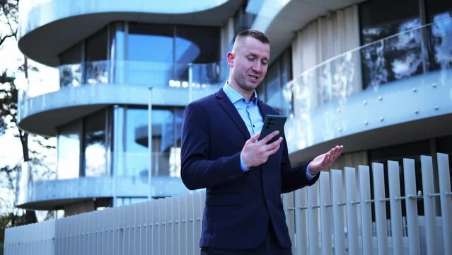Businessman in business attire is absorbed in a phone conversation, office building looming behind him. Each word Businessman speaks underscores his professionalism Device Communication Concept 