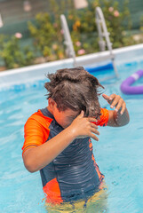 Boy in a swimming pool wipes his face, removing water after enjoying a refreshing swim