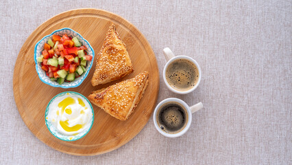 Puff pastry Bourekas with cheese, fresh yoghurt, vegetable salad, cups of coffee for kosher Israeli breakfast.