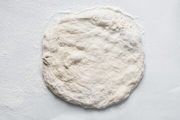 Overhead view of bread dough on parchment lined baking sheet, Shaping proofed dough on a white surface, process of making artisan bread