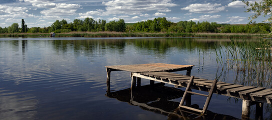 Fishing bridge. Spring clouds along the pond.Recreational area. Fishing grounds. Pond and recreation area.