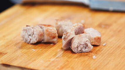 A close up of a piece of meat with a knife on a wooden cutting board. The meat is cut into small pieces and he is raw