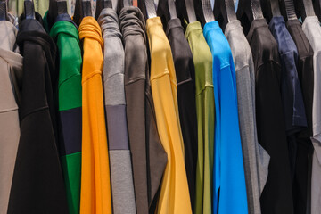 A rack of clothes with a variety of colors including yellow, green, blue, and black. The clothes...