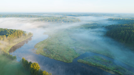 A foggy morning over a river with trees in the background. The sky is a light blue color