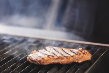 A piece of meat is on a grill, with the grill marks visible. The meat is brown and he is cooked. Concept of anticipation and excitement, as the meat is being prepared for consumption