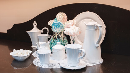 A white tea set is displayed on a counter with a lace doily. The tea set includes a teapot, cups,...