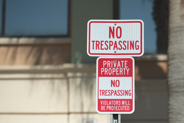 Rectangle image of a red and white no trespassing sign screwed to a metal post.