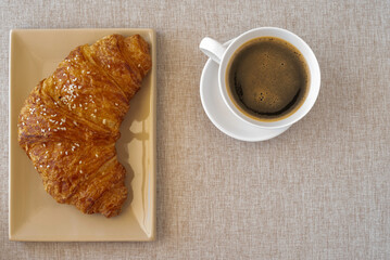 Fresh croissant and cup of coffee for tasty breakfast on cotton fabric background..