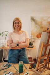 Portrait of female artist at atelier with arms crossed smiling at camera