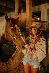 Portrait of young rancher girl in stall at ranch petting at horse.