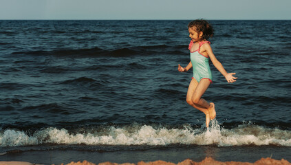 Portrait of jumping laughing girl of 5 years in blue swimsuit runs in sea water