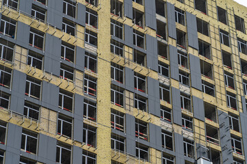 Concrete wall with attached aluminum holders or brackets for heat insulation of mineral wool. Monolithic frame of apartment building under construction with partially attached facade cladding blocks