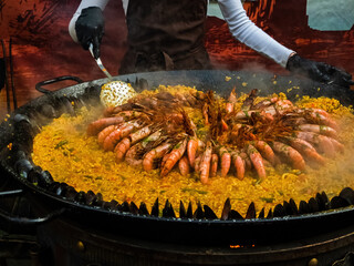 female chef cooking paella with rice, shrimp and shellfish in a large cauldron, street food