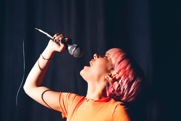 A woman singing into a microphone with pink hair. young woman sings enthusiastically and playfully