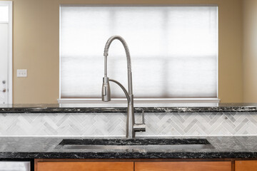 A kitchen faucet detail with wood cabinets, a black granite countertop, herringbone tile...