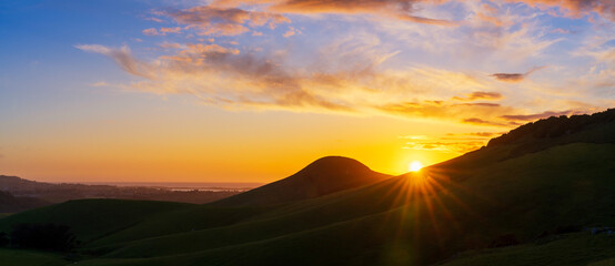 Silhouetted hills with sunburst, at sunset, sunrise