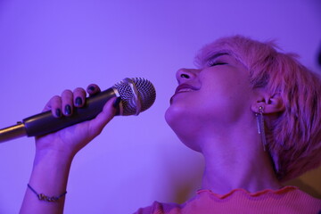A woman singing into a microphone with pink hair. young woman sings enthusiastically and playfully