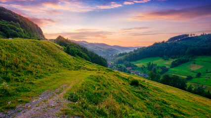 village in the valley between grassy hills at sunrise. beautiful rural landscape of transcarpathia, ukraine. nature scenery with red clouds above carpathian mountains